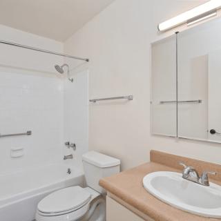 A modern bathroom featuring a bathtub with a shower, a sink with a mirror cabinet, and white walls.