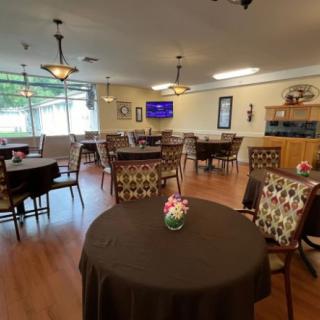 A cozy dining area with elegantly arranged tables and chairs, featuring flower centerpieces and warm lighting.
