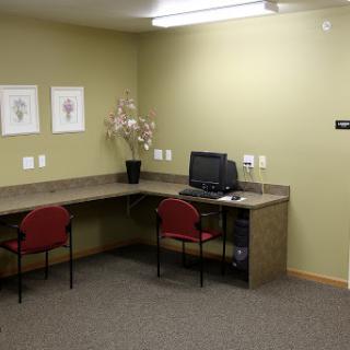 A tidy office workspace featuring a desk with a computer and two red chairs, set against green walls.