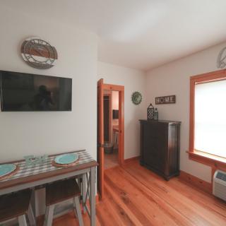 A cozy dining area with a table and two chairs, a wall-mounted television, and natural light from a window.