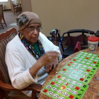 An elderly woman playing bingo indoors, enjoying a leisure activity.