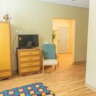 A cozy bedroom with wooden furniture, including a wardrobe and dresser, a TV, and a chair near an open doorway.