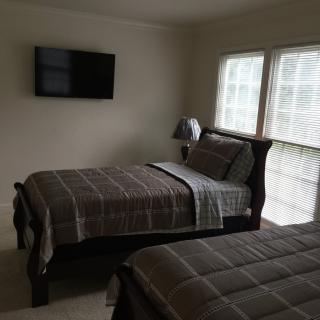 A cozy bedroom with two twin beds, a wall-mounted television, and large windows letting in natural light.