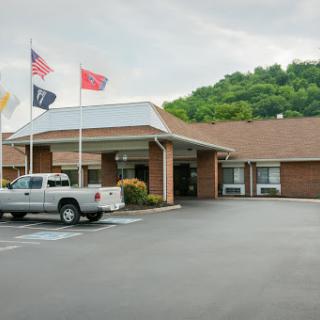 A view of a hotel entrance with several flags and parked vehicles.