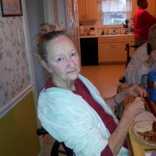 A woman seated at a table preparing food in a kitchen.