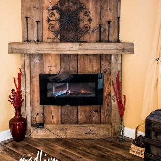 A rustic fireplace with wooden paneling, adorned with candles and decorative vases, creates a cozy atmosphere.