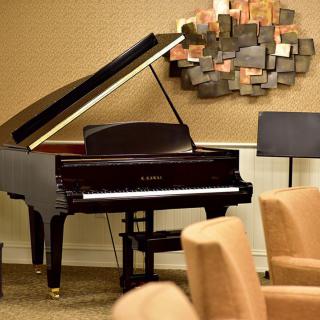 A grand piano in a cozy room with art on the wall and comfortable seating.