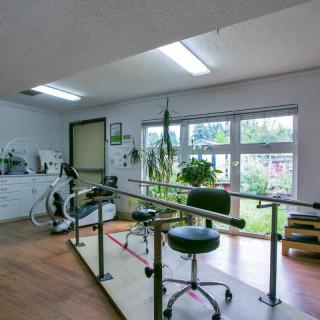 A physical therapy room equipped with parallel bars and exercise equipment, featuring bright natural lighting.