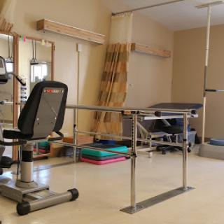 A well-equipped rehabilitation therapy room featuring exercise equipment and balance bars for patient assistance.