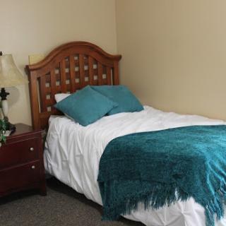 A cozy bedroom featuring a single bed with teal accents and wooden furnishings.