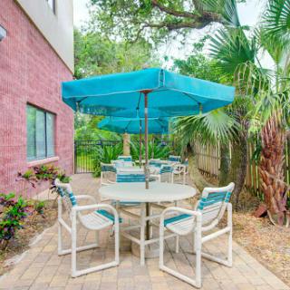 A cozy outdoor seating area with a table, chairs, and an umbrella surrounded by lush greenery.