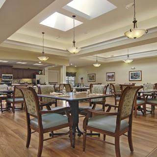 A spacious dining room with elegant tables and chairs arranged under warm lighting and skylights.