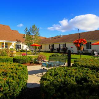 A beautiful garden with neatly trimmed bushes and vibrant flowers set in front of a large building under a clear blue sky.