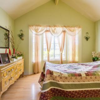 A cozy bedroom with soft green walls, a large window adorned with curtains, and a quilted bedspread on a neatly made bed.