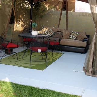A cozy outdoor patio setup with a sofa, chairs, table, and a green rug under a canopy.