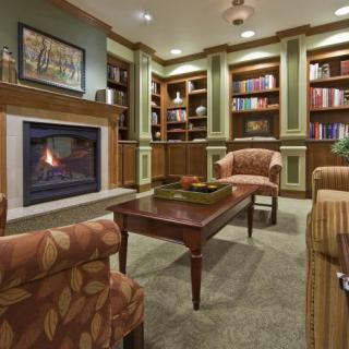 A cozy library room featuring a fireplace, comfortable seating, and bookshelves filled with books.