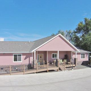 A pink suburban house with a front porch and driveway, surrounded by trees on a clear day.