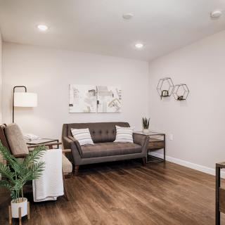 A modern and minimalist living room with a cozy sofa, hardwood floors, decorative wall art, and an indoor plant.
