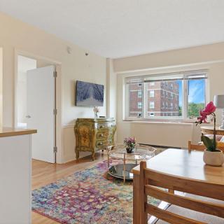 A cozy living room with a large window, wooden floors, and colorful decor.