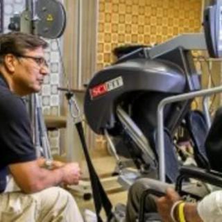 A trainer interacting with a person using exercise equipment in a gym setting.
