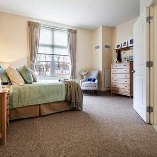 A cozy bedroom with a well-made bed, soft carpet, and ample natural light.