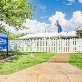A welcoming community center with a white picket fence and flags waving under a bright blue sky.