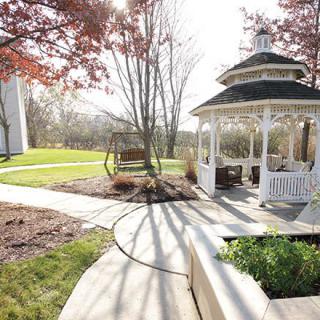 A scenic garden featuring a gazebo, swing, and winding pathways under a clear sky.