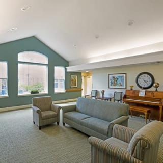 A spacious living room with sofas, chairs, and a piano under soft lighting.