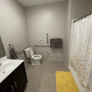 A modern and accessible bathroom with a toilet, sink, and shower featuring a handrail.