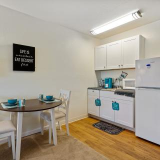 A cozy, modern apartment kitchen with a small dining area featuring white cabinets and wooden flooring.