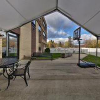 A spacious patio with outdoor seating, a portable basketball hoop, and a view of the backyard under a cloudy sky.
