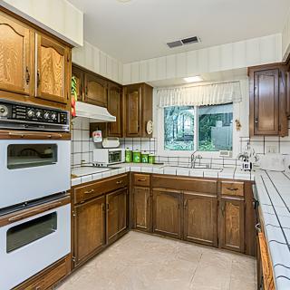 A retro-style kitchen with wooden cabinets, tile countertops, and a double oven.