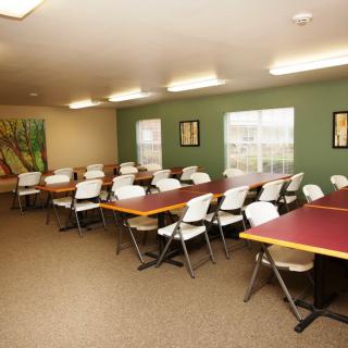 An empty classroom with tables and chairs arranged neatly, featuring artwork on the walls.