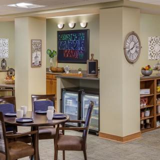 A cozy dining area with a central table and chairs, featuring modern decor including wall art and a clock.