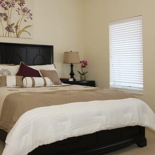 A cozy bedroom with a neatly made bed, bedside lamp, and window blinds.