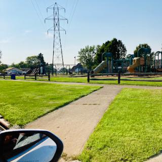 A sunny day at the park featuring a playground and lush green grass.
