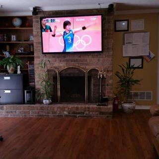 A cozy living room with a television displaying an Olympic sports event, set above a brick fireplace.