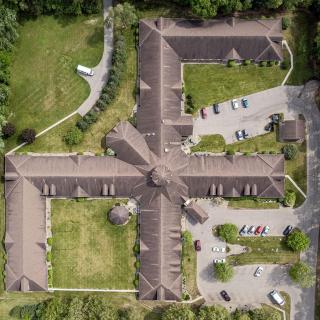 Aerial view of a symmetrical building surrounded by greenery and a parking lot.