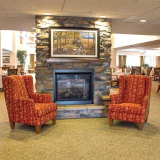 A cozy lounge area featuring a stone fireplace flanked by two red patterned chairs.