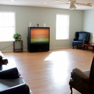 A minimalist living room featuring a vintage TV, wooden flooring, and armchairs with ample natural light.