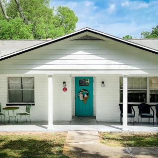 A charming single-story house with a white facade and a teal front door, featuring outdoor seating on the porch.