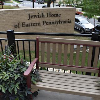A view of the Jewish Home of Eastern Pennsylvania, featuring a bench in front of the building.