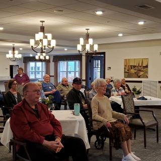 A group of seniors attentively listening during a community meeting indoors.