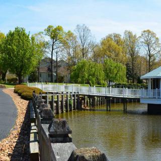 A peaceful lakeside scene with a dock, trees, and a house in the background.