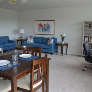 A cozy living and dining area featuring blue sofas, a dining table, and a bookshelf.