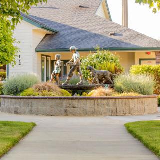 A garden with a sculpture of children and a dog in front of a house.
