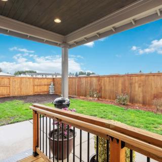 A view from a covered patio overlooking a fenced backyard with a grassy lawn and a grill on the deck.
