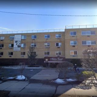 A four-story residential apartment building with multiple windows and a central entrance, set in an urban environment.
