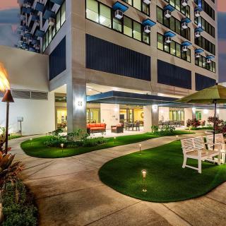 A beautifully lit hotel exterior with a landscaped garden and outdoor seating area at night.