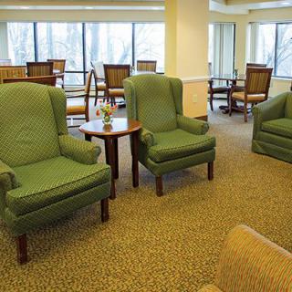 A cozy lounge area with green upholstered chairs and tables by large windows.